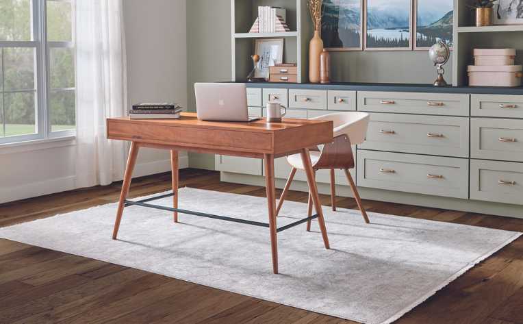 dark hardwood floor in sage green modern home office with wood desk and area rug